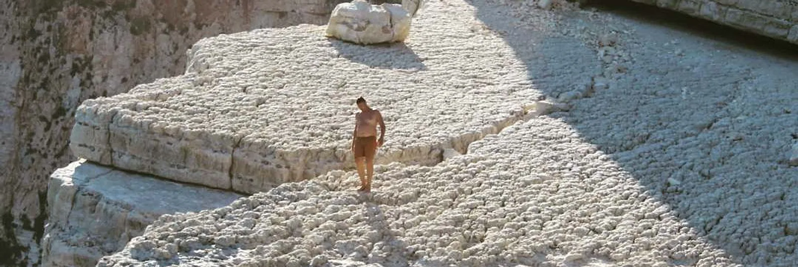 Lone figure walking across pale rocks in bright sunlight, photograph by Dawn O’Donoghue New Day Therapies